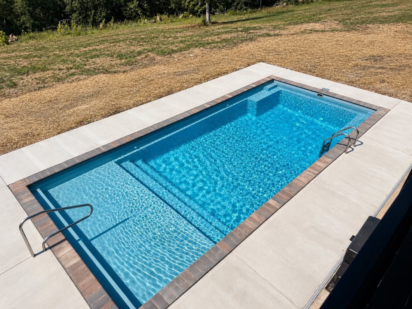 Rectangular fiberglass pool with paver coping and a new concrete deck by No Limit Signature Pools
