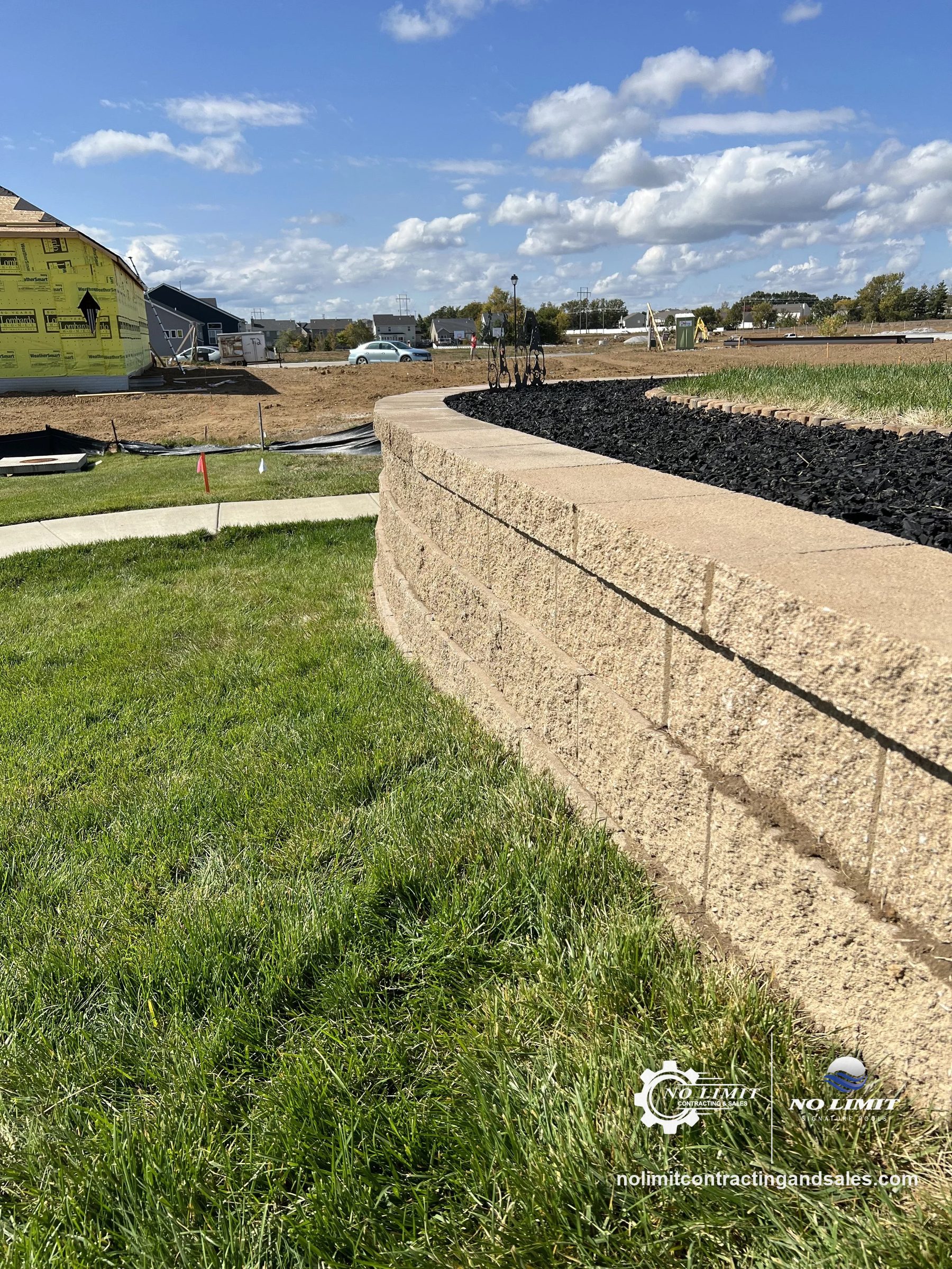 Curved tan block retaining wall with black mulch bed, new subdivision by No Limit Contracting & Sales