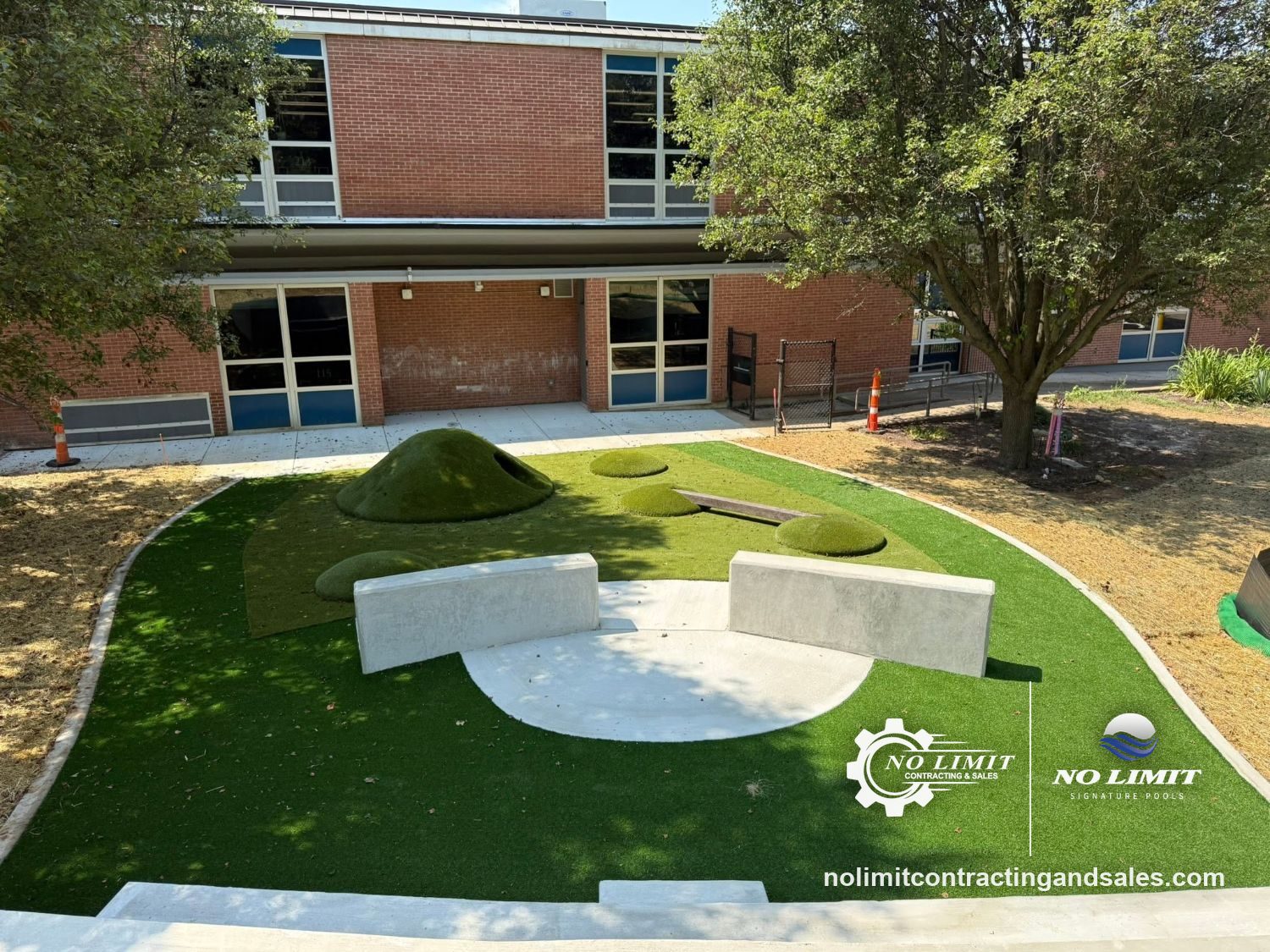 School courtyard with concrete seat walls, a round concrete pad and turf play mounds by No Limit Contracting & Sales