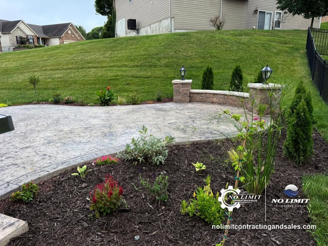 Stamped concrete patio with a block seat wall and lantern pillars by No Limit Contracting & Sales