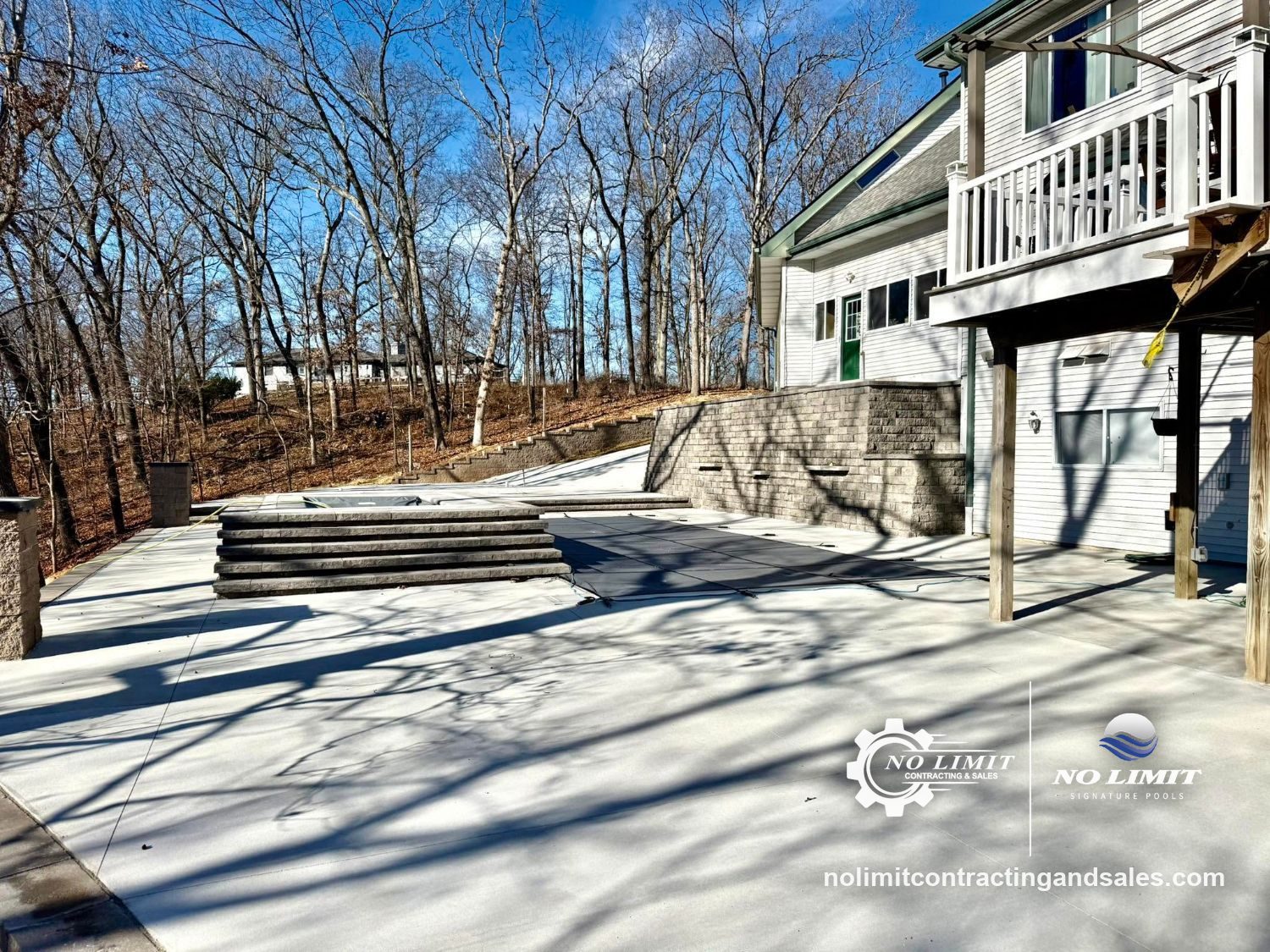 Covered pool with a wide concrete deck, stepped block seating and tall block retaining wall by No Limit Contracting & Signature Pools