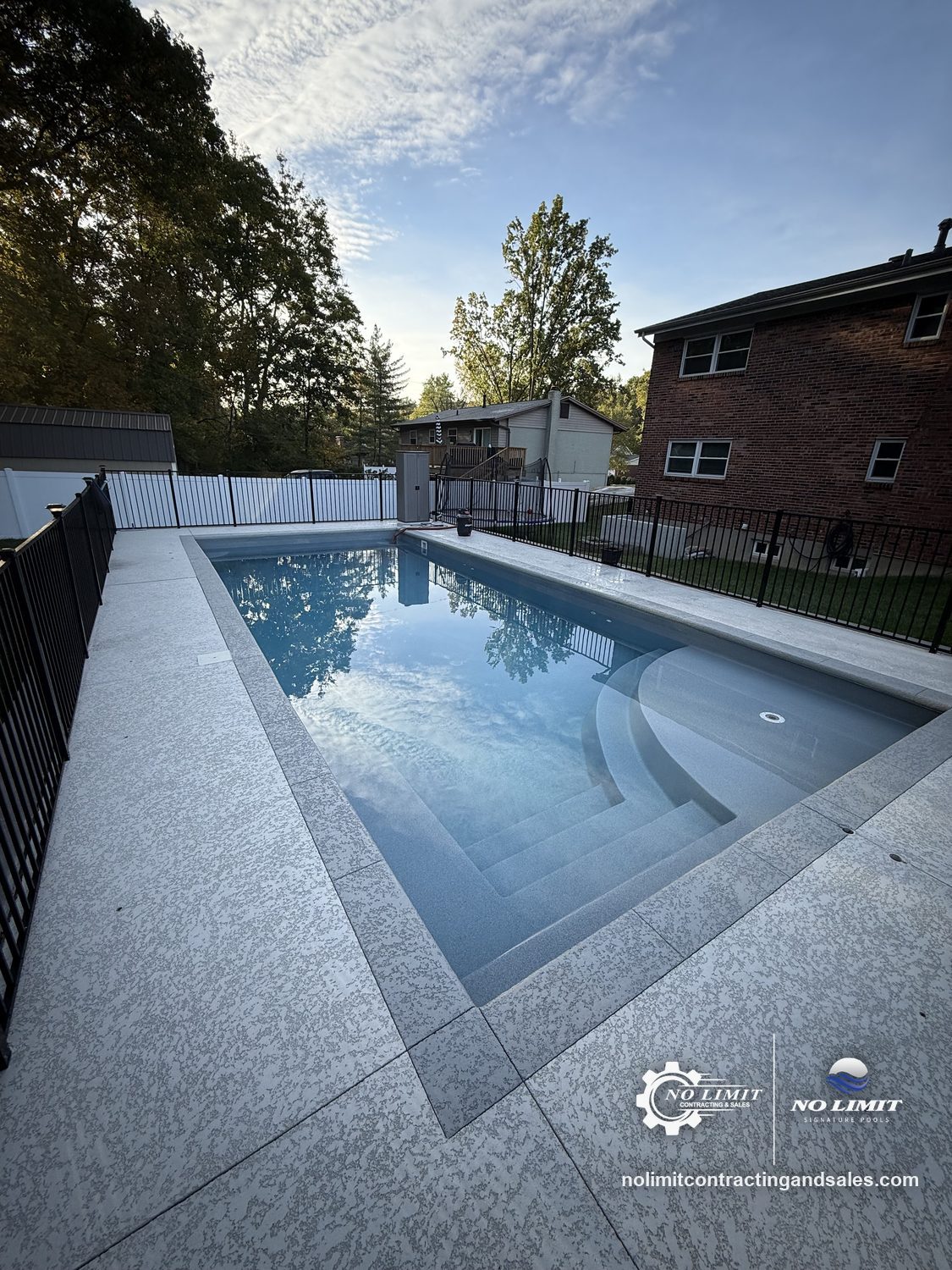 Finished rectangular fiberglass pool with entry steps and black fence at golden hour by No Limit Signature Pools