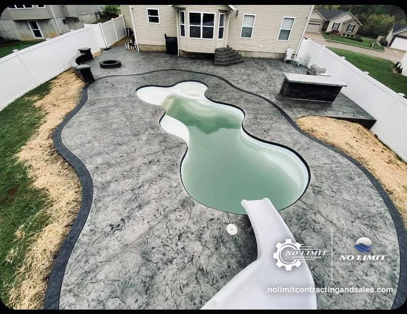 Freeform fiberglass pool with gray stamped concrete deck, slide and outdoor bar by No Limit Signature Pools