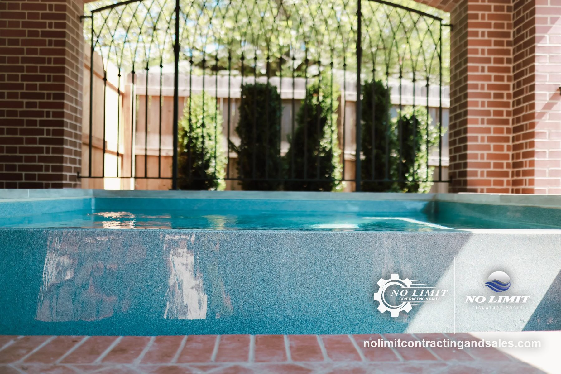 Raised spa wall with teal finish, brick pillars and iron gate by No Limit Signature Pools
