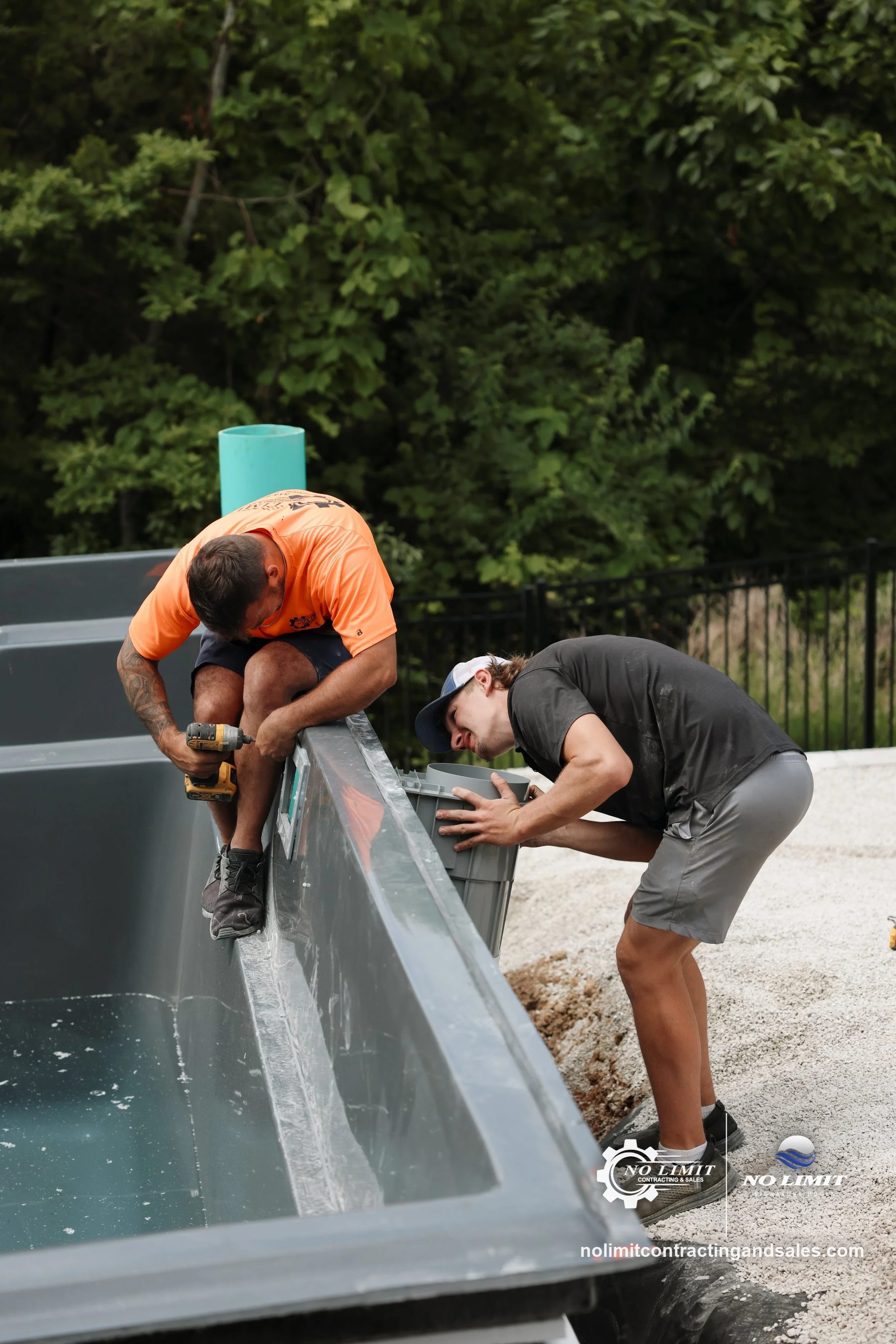 Two crew members setting a gray fiberglass pool shell during install by No Limit Signature Pools